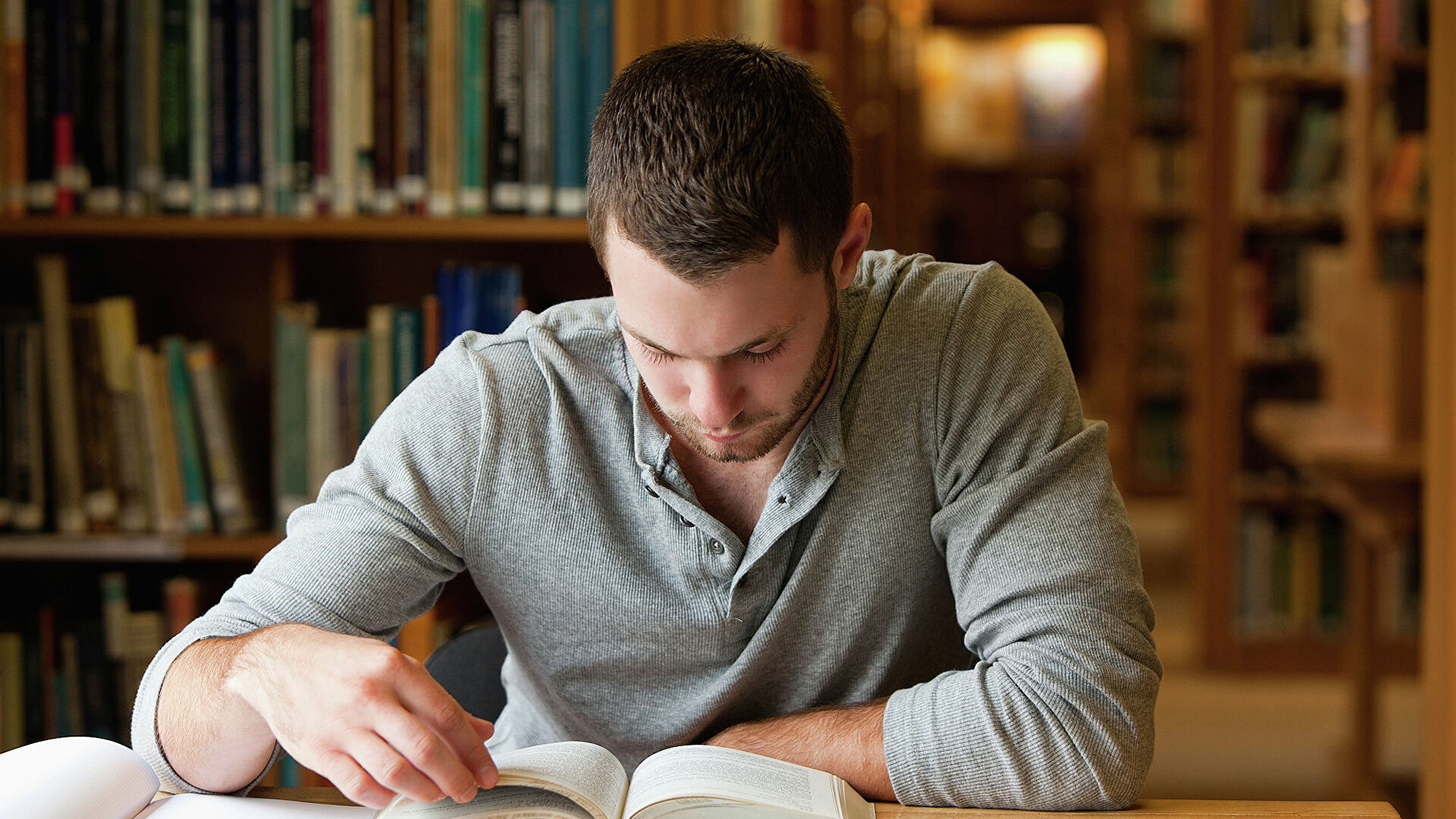 Человек читает книгу в библиотеке, изучая публикации с концентрированным лицом.